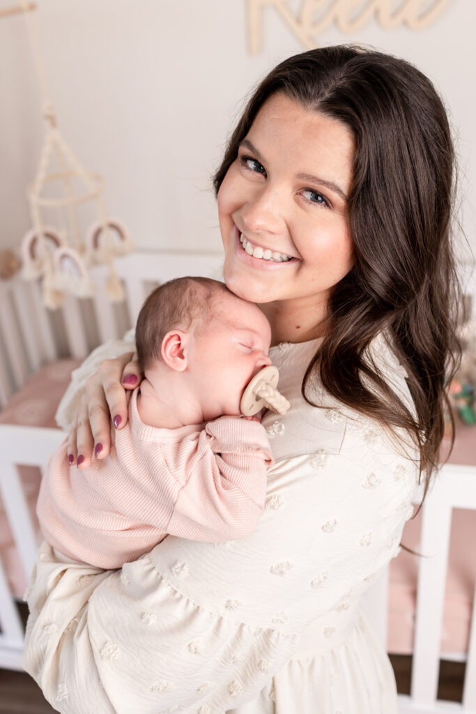 A new mom holding her baby in the nursery during their in-home newborn photography session.