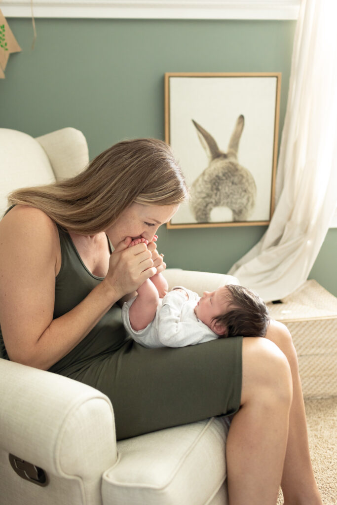 A mom sitting in a rocking chair in the nursery kissing her baby boy during their in-home newborn photography session.
