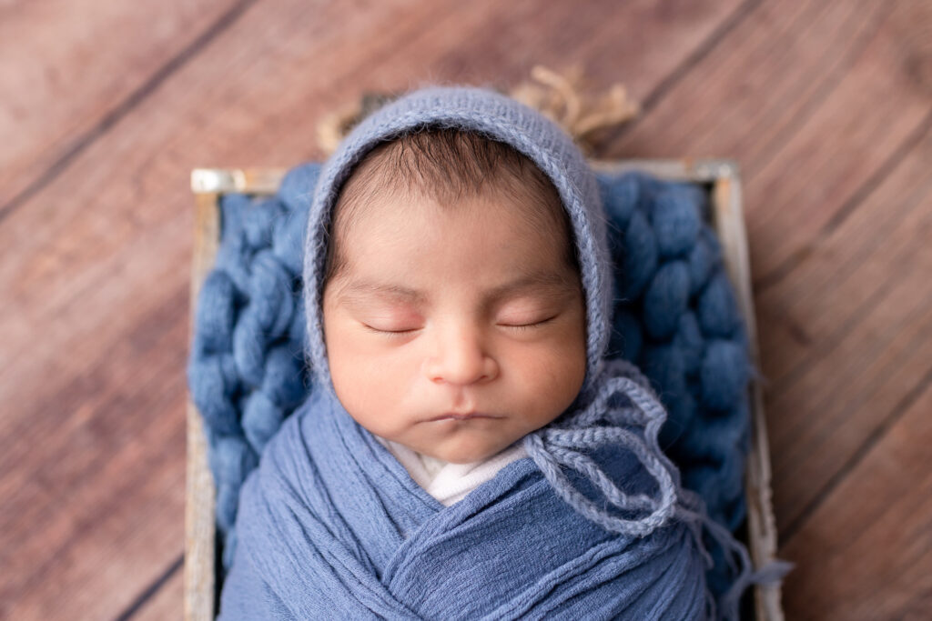 Baby boy in a wrap and bonnet posed in a prop during his in-home newborn photography session in Frankfort, Kentucky.